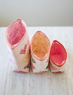 three paper cups sitting on top of a white wooden table covered in pink and orange fabric