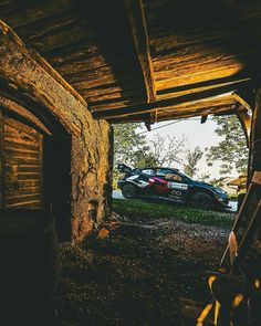 a car is parked in an old wooden structure with grass and trees around it,