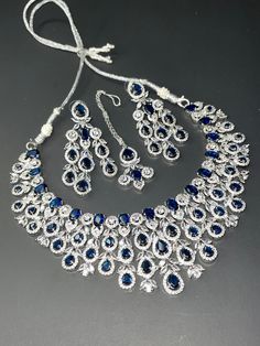 This beautiful AD set is a masterpiece of elegance and sophistication. The premium quality silver base is adorned with vibrant sapphire stones, carefully set to create a stunning visual effect. The set includes: - A delicate necklace featuring a sapphire stone pendant, suspended from a dainty silver chain - A beautiful tikka or headpiece, showcasing a sapphire centerpiece, perfect for adding a touch of glamour to any outfit - Dainty earrings, featuring sapphire accents, adding a subtle yet stylish finishing touch The silver base provides a sleek and modern contrast to the rich, luxurious sapphire stones, creating a truly eye-catching combination. The set is carefully crafted to ensure a comfortable and secure fit, making it perfect for everyday wear or special occasions. With its unique bl White Gold Sapphire Jewelry With Sparkling Stones, Sapphire Sterling Silver Jewelry Hand Set, Luxury Hand-set Sapphire Jewelry, Elegant Hand Set Sapphire Jewelry, Sapphire Jewelry With Stones In White Gold, Elegant Hand-set Sapphire Jewelry, Sapphire Stones White Gold Jewelry, Luxury Sapphire Jewelry With Sparkling Stones, White Gold Sapphire Jewelry With Stones