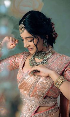 a woman in a pink and gold sari with jewelry on her neck, looking down