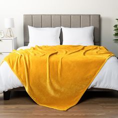 a bed covered in a yellow blanket next to white pillows and a potted plant