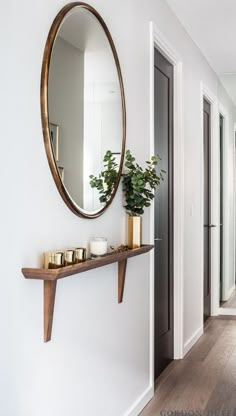 a mirror on the wall next to a shelf with candles and a potted plant