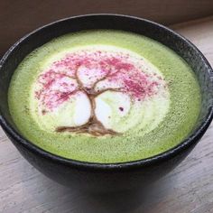 a cup filled with green liquid and a tree painted on the top in pink ink