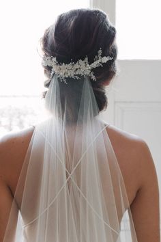 the back of a bride's head wearing a veil with flowers and pearls on it