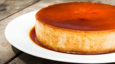 a cheesecake covered in caramel sauce on a white plate with a wooden table