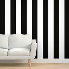 a white couch sitting in front of a black and white wall with vertical stripes on it