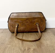 1970's vintage brown tan tooled leather boho embossed floral handbag/purse/bowling bag with two overarm straps and an outside open pocket   The bag fastens with a zip.  The inside of the bag has one main compartment Bag measurements: 37cm x 23.5cm x 15cm  Strap length: 54cm  There are some marks to the leather and some of the tooling has come apart at the bottom of the bag (please see pictures), but otherwise in good vintage condition  For more information or pictures please ask  WORLDWIDE SHIPPING  Click here for more vintage pieces www.etsy.com/shop/vintagejemsbyjane Vintage Leather-backed Hobo Satchel Bag, Vintage Leather Hobo Bag With Top Handle, Vintage Leather Hobo Bag With Removable Pouch, Vintage Brown Hobo Bag With Leather Backing, Vintage Leather Hobo Bag, Brown Hand Tooled Clutch Bag, Vintage Clutch Bag With Adjustable Strap, Vintage Brown Top Handle Saddle Bag, Bohemian Brown Top Handle Shoulder Bag