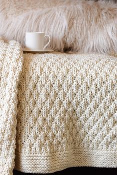 a coffee cup is sitting on top of a white knitted blanket that has been folded over