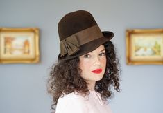 "DESCRIPTION * Vintage hat from 1950s-1960s * women bowler hat design: tall round crown, narrowly curled up brim in the back and on the right    * made of brown wool felt fabric * the hatband is wrapped with a thick grosgrain ribbon and embellished a bow on the side * tag reads \"Electra/ Neumann Endler/ 100% Wool\" CONDITION * the hat has a few indented and insect bite marks on the brim, please see the last photo. * otherwise, the hat shows signs of normal use with minor soiling, discoloration Retro Short Brim Top Hat For Kentucky Derby, Vintage Fedora With Flat Brim For Parties, Retro Fedora Hats For Kentucky Derby, Vintage Fedora Hat For Kentucky Derby, Vintage Brown Boater Hat With Short Brim, Retro Short Brim Hat For Kentucky Derby, Vintage Brown Mini Hat With Flat Brim, Retro Brimmed Felt Hat, Vintage Brimmed Fedora For Party