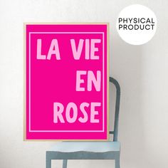 a pink poster with the words la vie en rose on it in front of a blue chair