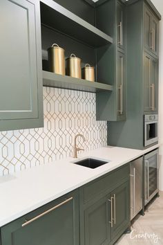 a kitchen with green cabinets and white counter tops, gold accents on the backsplash