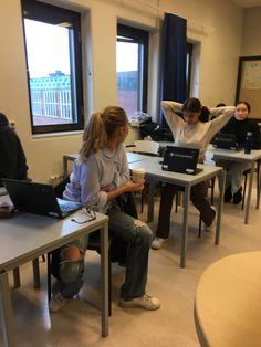 several people sitting at desks with laptops on their laps and one woman stretching her arms behind her head