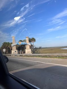 an airplane flying over the top of a building on a highway with palm trees in front of it