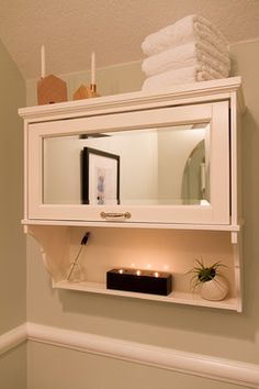 a white shelf with some candles and pictures on it in a bathroom next to a toilet