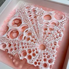 an intricately designed piece of paper in a pink box with holes and circles on it