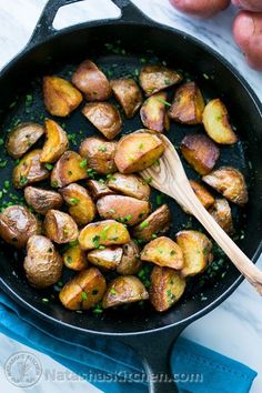 cooked potatoes in a skillet with a wooden spoon on the side and fresh parsley