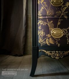 a purple and gold painted chest of drawers with flowers on the front, in a room