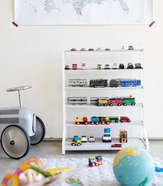 a white shelf filled with toy cars next to a wall mounted map