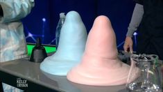 two people are standing near some fake plastic cones on a tv set, and one person is holding a remote control