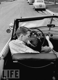 a man driving a car with a child in the back seat and his arm on the steering wheel