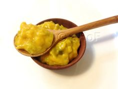 a wooden spoon filled with yellow food on top of a white table next to a bowl