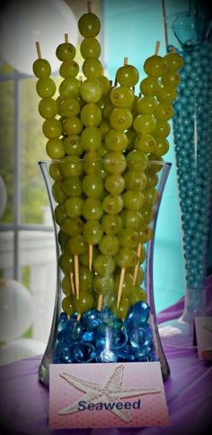 a vase filled with green grapes on top of a purple table next to blue and white candy