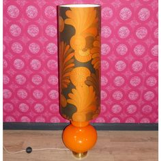 an orange vase sitting on top of a wooden floor next to a pink wall with circles