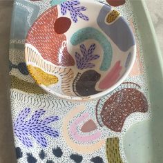 a colorful bowl sitting on top of a table next to a plate with designs on it