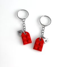 two lego keychains are attached to each other on a white surface, one is red and the other is silver