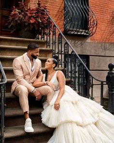 a man and woman sitting on the steps in front of some stairs wearing wedding dresses