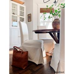 a dining room table with two white chairs and a brown bag