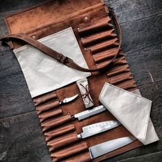 an assortment of kitchen utensils and knives laid out on a table with leather pouch