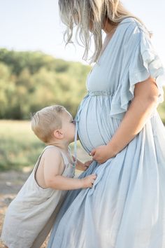 a pregnant woman in a blue dress is holding her toddler's belly