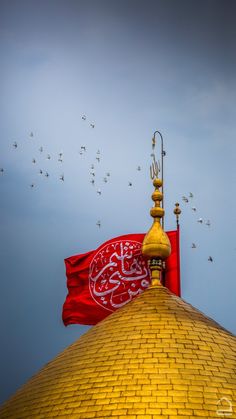 a large red flag on top of a yellow building with birds flying in the sky