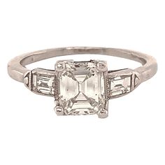 Art Deco period celebrates a keen sense of modernity. One hundred years later, it is still one of the most sought-after jewelry periods. This emerald cut diamond (1.03 cts., J, VS) highlights the geometric lines of the time. Flanked by two baguette cut diamonds in a bullet shape bezel with milgrain engraving. Set in platinum. Size 6 and can be custom-sized. Box not included. Alice Kwartler has sold the finest antique gold and diamond jewelry for over forty years. 1920s Engagement Ring Vintage, 1920s Engagement Ring, Art Deco Diamond Ring Engagement, Antique Diamond Engagement Rings, Edwardian Engagement Ring, Platinum Engagement Ring, Platinum Diamond Engagement Rings, Art Deco Engagement, Emerald Cut Diamond