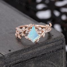 an opal and diamond ring sitting on top of a wooden table with black background