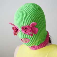 a woman wearing a green knitted hat with pink flowers on the top and bottom