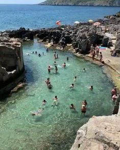 many people are swimming in the water near some rocks