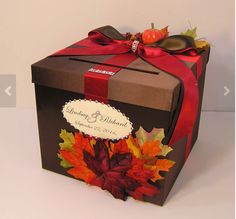 a gift box with a red ribbon and autumn leaves on the front, sitting on a white surface