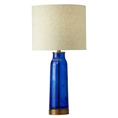 a blue glass table lamp with a white shade on the base and a beige linen lampshade