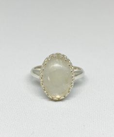 This cool, white Rainbow Moonstone gemstone ring reminds me of the puffy clouds that accent a Spring day. After a rain you can see the dark clouds turn to wisps of white with a faint rainbow glistening through. This stone is just that! As you look at the ring and turn it you will see subtle flashes of blue purple and maybe green. The lovely way the stone is nestled within the Sterling silver scalloped bezel setting gives this special piece a dainty yet bold look and feel. Designed in a timeless White Moon-shaped Opal Ring Gift, Adjustable White Moonstone Ring, White Moon Shaped Opal Ring For Gift, White Moon Shaped Opal Ring Gift, White Natural Stones Jewelry For Promise Ring, Minimalist White Crystal Ring With Gemstone, Minimalist White Crystal Gemstone Ring, White Moon-shaped Opal Gemstone Ring, White Moon Shaped Opal Gemstone Ring