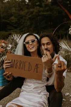 a bride and groom sitting on the ground holding up a sign that says married af