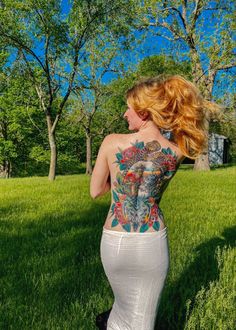 a woman with tattoos on her back standing in the grass