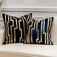 two black and gold pillows sitting on top of a white couch next to a potted plant