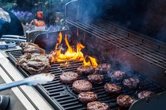 hamburgers and burger patties cooking on the grill with flames in the foreground