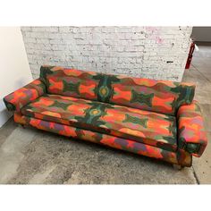 an orange and green couch sitting in front of a brick wall