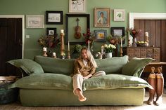 a woman sitting on top of a green couch in a living room next to pictures