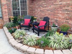 two chairs sitting on top of a patio surrounded by plants and potted plants in front of a brick building