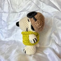 a crocheted stuffed animal holding a yellow object on a white sheet with a black hat