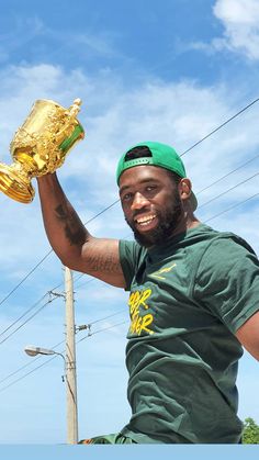 a man in green shirt holding up a gold object with one hand and another arm